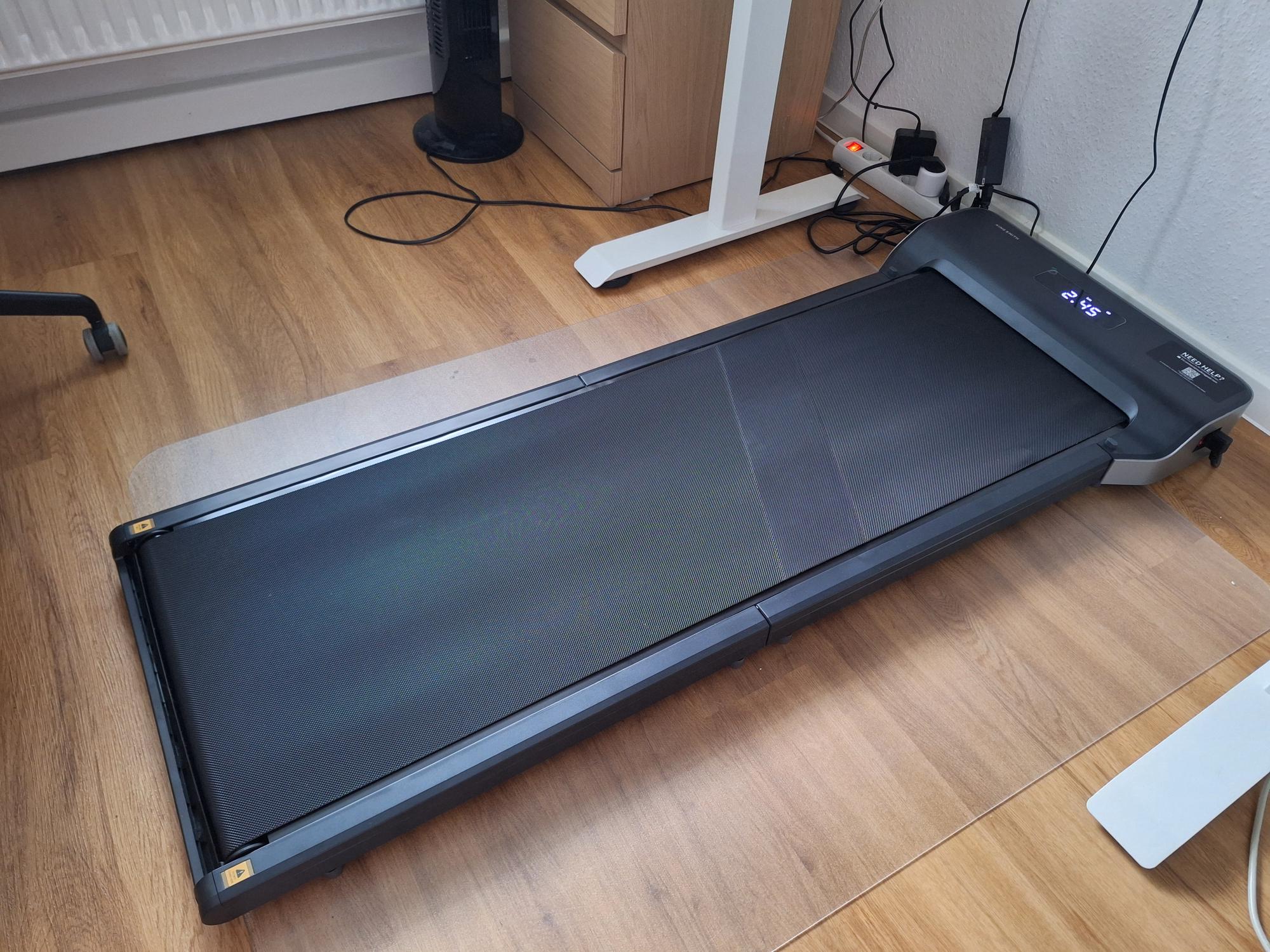 My new walking pad under my standing desk AI generated caption: Treadmill on wooden floor near desk.